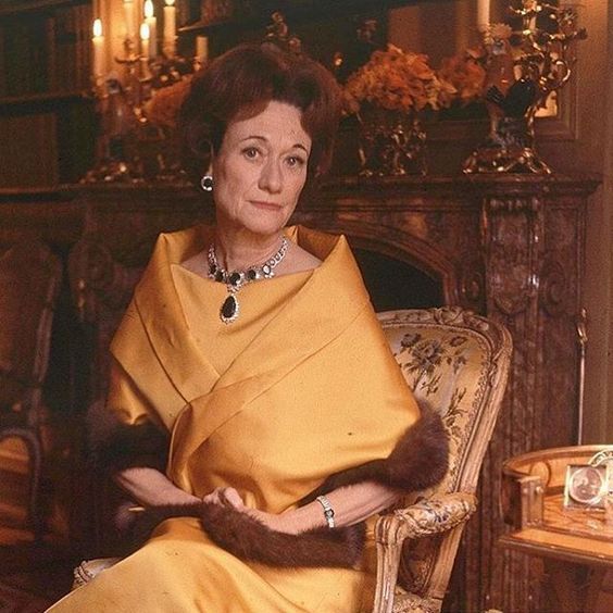 an old photo of a woman in a yellow dress sitting on a chair with a fur stole around her neck