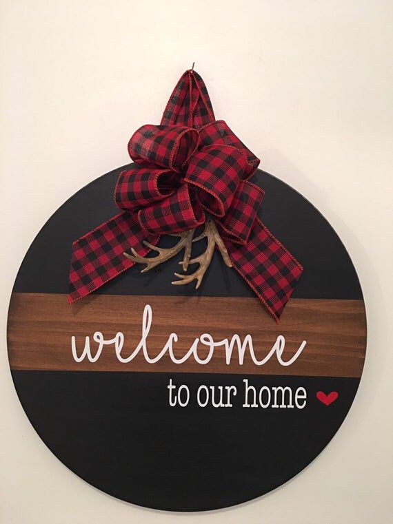 a welcome sign hanging on the wall with a red and black ribbon tied around it