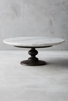 a white marble cake plate on a wooden stand in front of a gray wall and floor