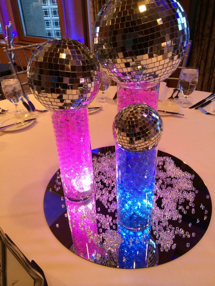 two disco balls sitting on top of a table with purple and blue lights around them