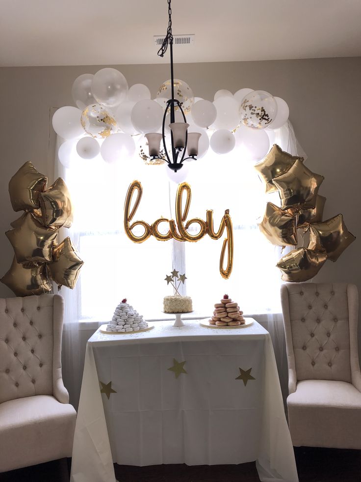 a baby shower table with balloons and gold stars on it, next to two chairs