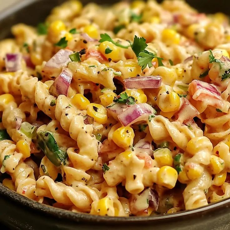 a bowl full of macaroni salad with onions, corn and cilantro