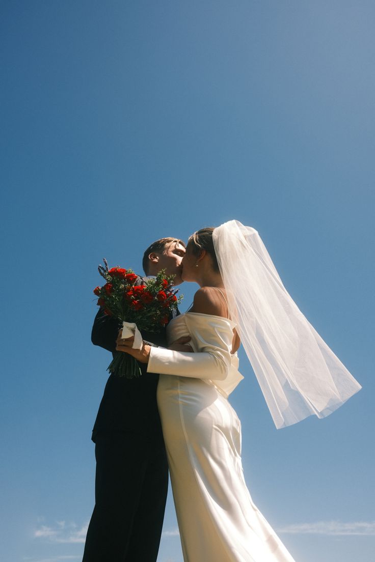 a bride and groom kissing in front of a blue sky