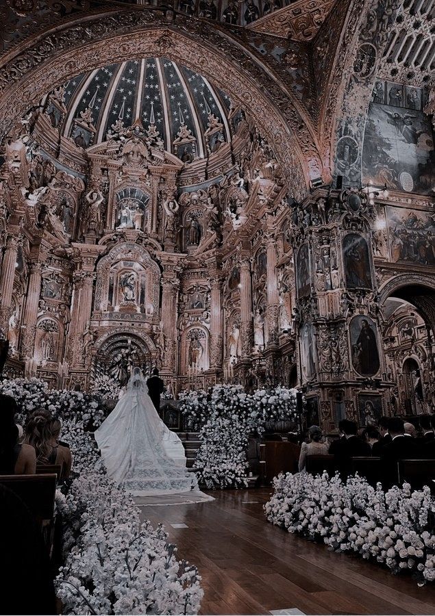 the bride is walking down the aisle in her wedding dress at the alter, surrounded by white flowers