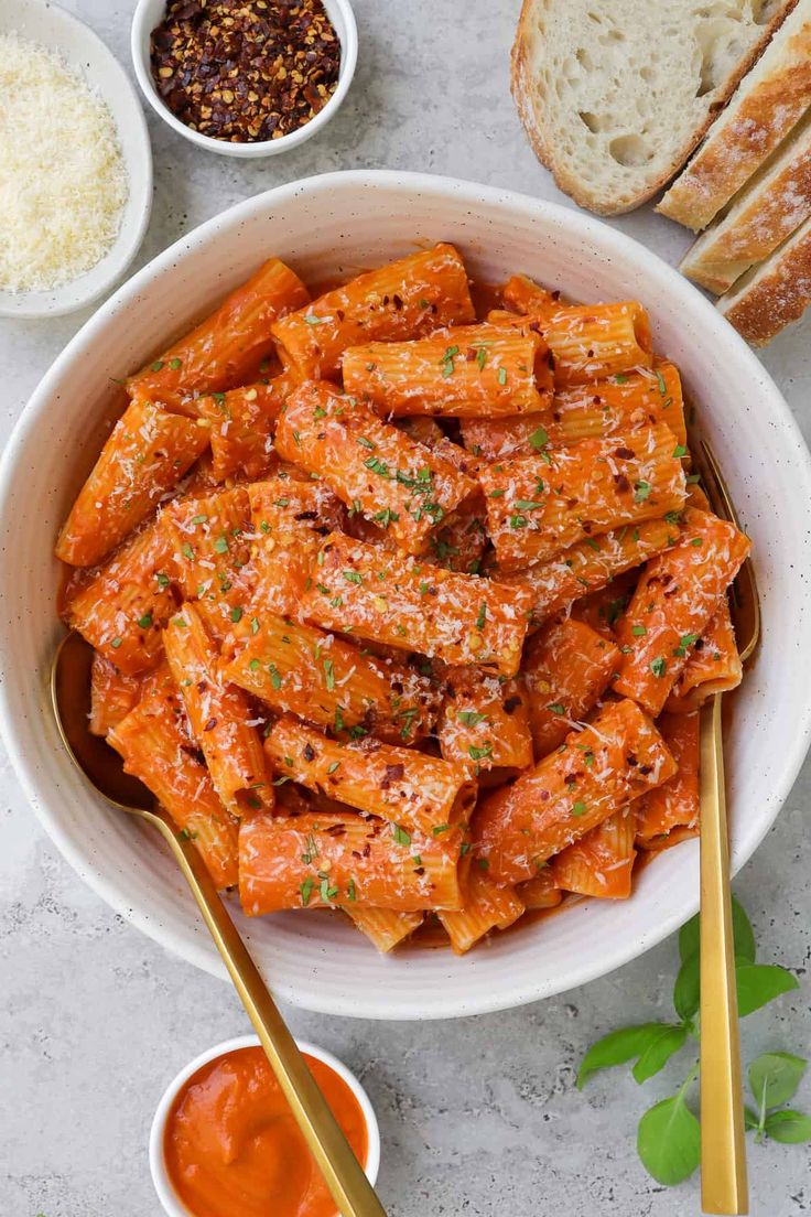 a white bowl filled with pasta next to bread and dipping sauces on a table