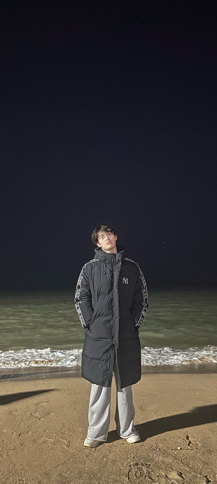 a man standing on top of a sandy beach next to the ocean under a dark sky