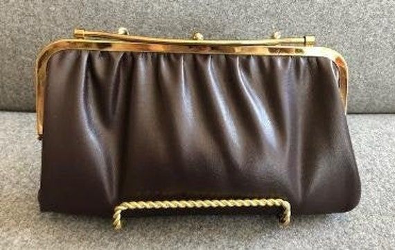 Stylish mid century brown leather clutch with gold frame and a unique closure.  It has a curved gold bar on top which snaps shut over the one ball clasp.  Very clever and elegant.  Inside is lined in a taupe leather.  The leather is soft and supple. There are no tags or markings in the bag.  Measuring 10 1/2" inches in length and 6" inches in height it is in excellent vintage condition.  There is one small pen mark on the inside. Please refer to photos for details.  We use recycled material when Brown Leather Clutch, Vintage Scarves, Taupe Leather, Vintage Silk Scarf, Small Pen, Mid Century Vintage, Vintage Scarf, Gold Bar, Vintage Silk