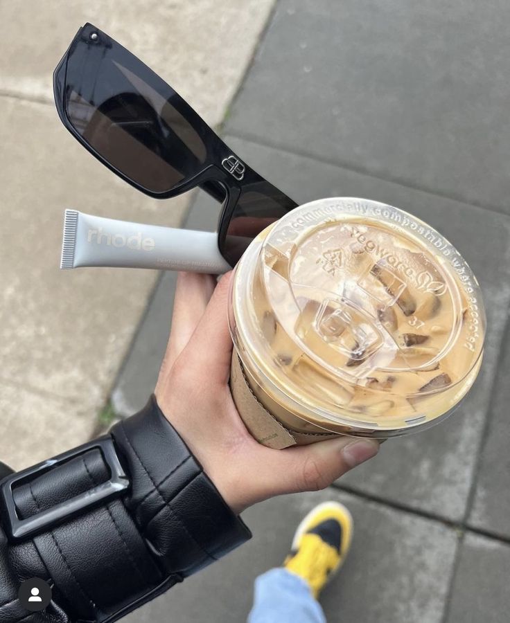 a person holding up a cup of coffee and sunglasses