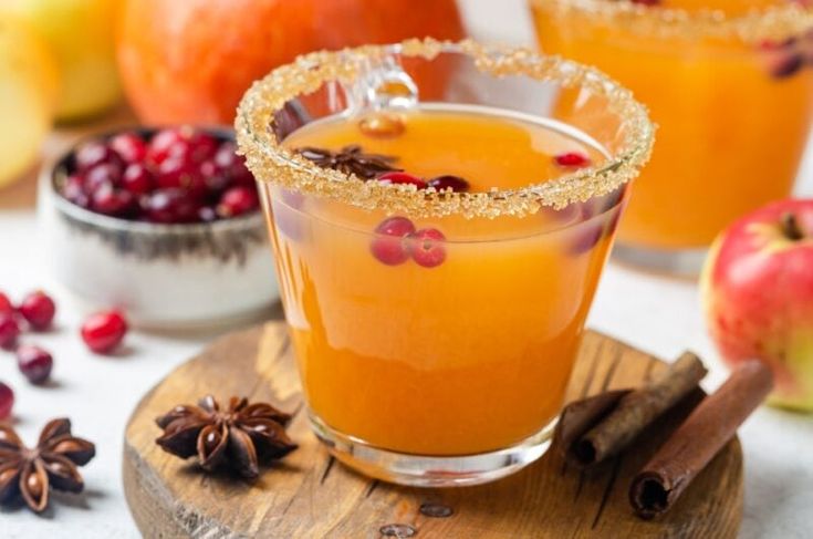 two glasses filled with apple cider on top of a wooden board