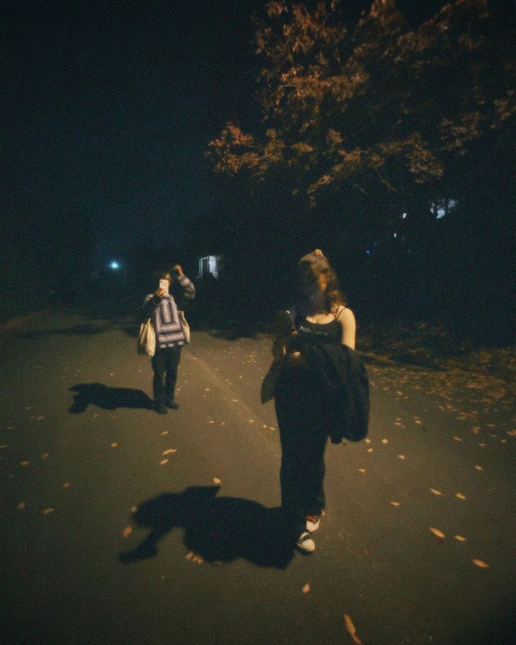 two people walking down the road at night with one person taking a photo on his cell phone