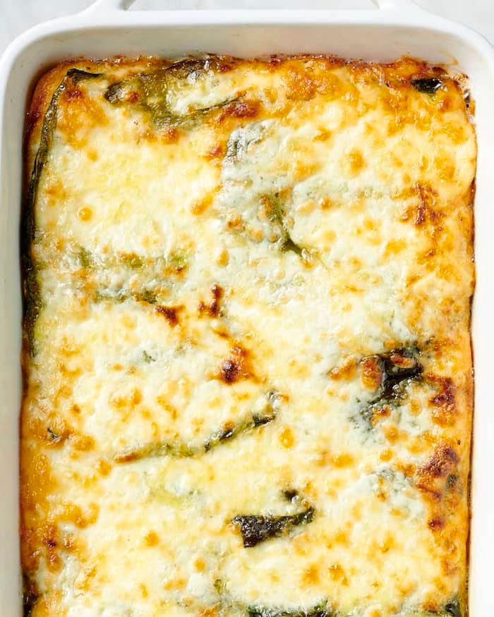 a casserole dish with cheese and spinach in it on a white surface