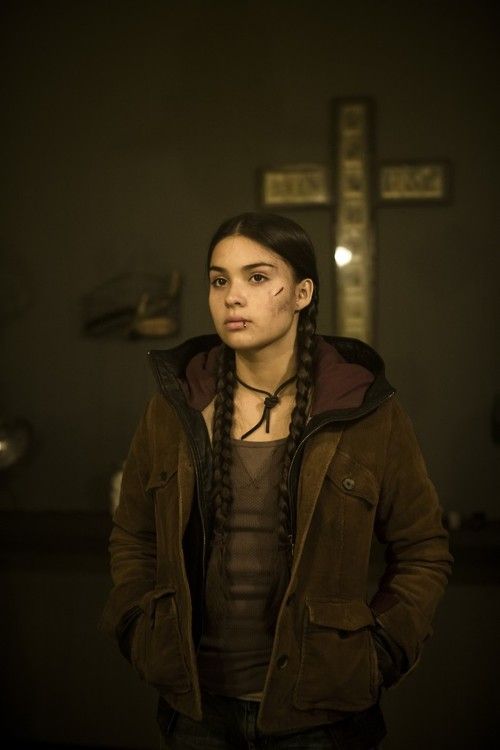 a woman with long braids standing in front of a cross and looking at the camera