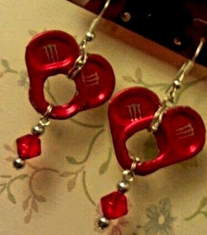 two red heart shaped earrings with beads hanging from the hooks on a wall next to a mirror