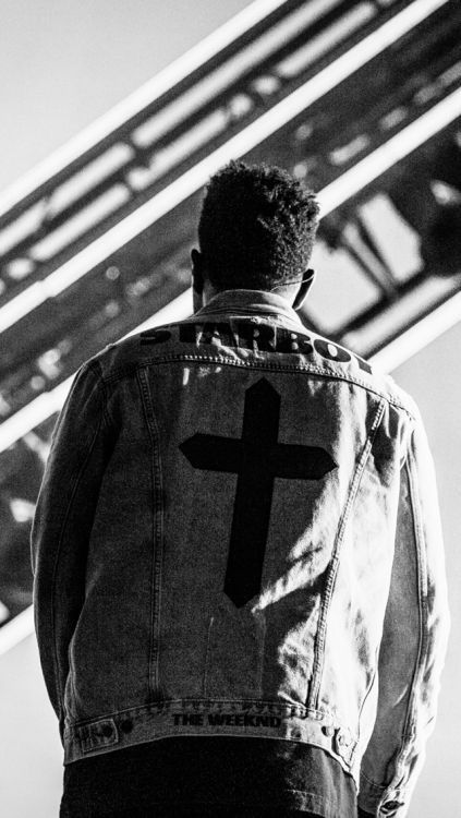 a man wearing a jean jacket with a cross on the back, standing in front of some stairs