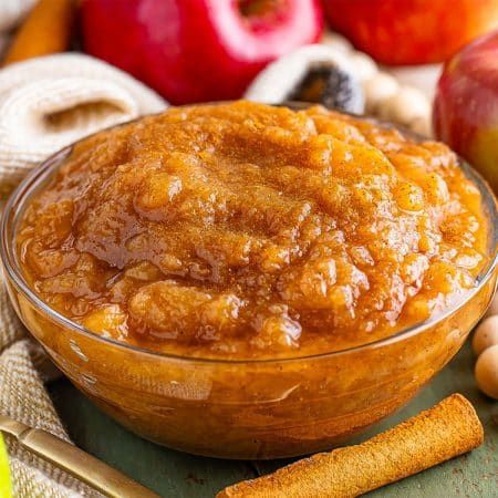 an apple pie in a glass bowl surrounded by apples and cinnamon sticks