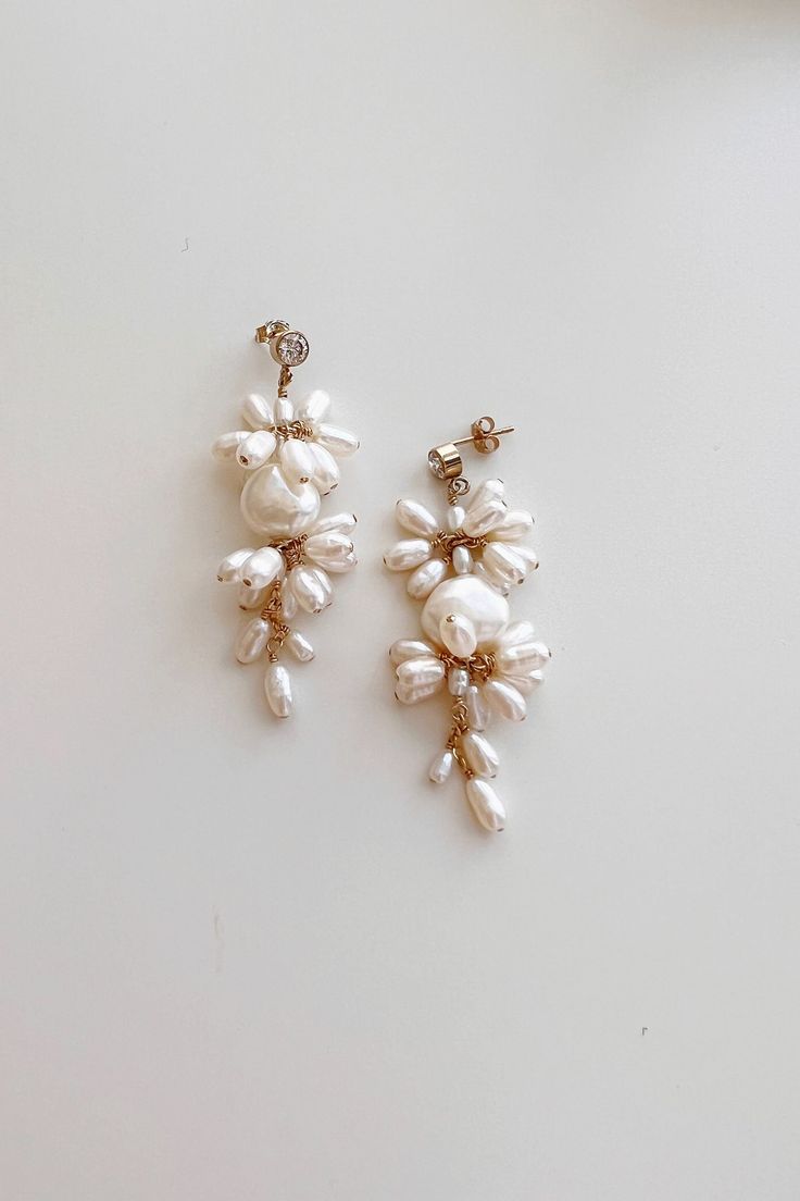 two pairs of earrings with pearls hanging from the end of each earring, on a white surface