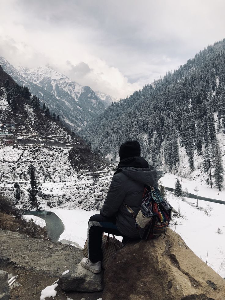 a person sitting on top of a rock looking out over a valley with snow covered mountains in the background