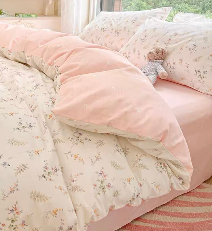 a bed with pink comforter and pillows on it in front of a large window