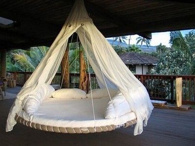 a white bed hanging from the ceiling in a room with wooden floors and palm trees