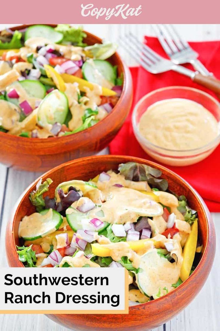 two wooden bowls filled with salad and dressing on top of a white wood table next to a red napkin