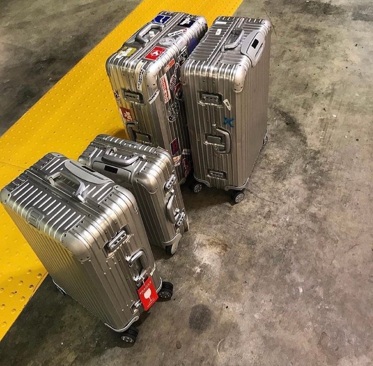 three silver suitcases sitting next to each other on a yellow and black striped floor