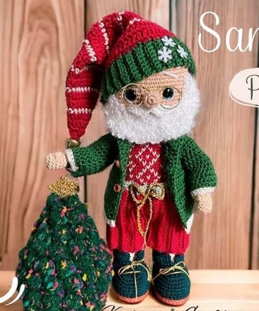 a crocheted santa clause doll holding a christmas tree ornament in front of a wooden background