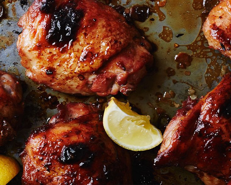 chicken thighs with lemons and sauce on a baking sheet