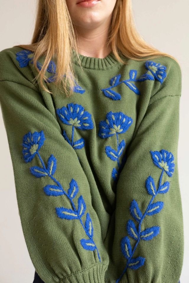 a woman wearing a green sweater with blue flowers on it