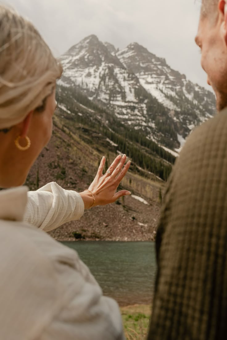 a man and woman standing next to each other in front of a mountain with snow on it