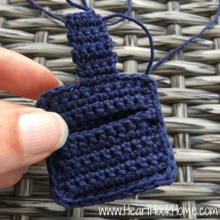 a hand holding a blue crocheted object on top of a woven table cloth