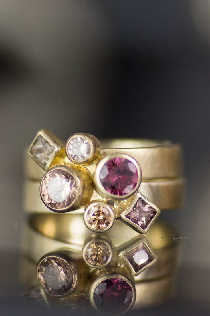 three gold rings with pink and white stones on the top one is set against a reflective surface