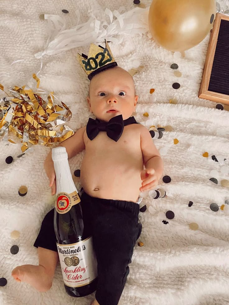 a baby wearing a crown and holding a bottle of champagne on top of a bed