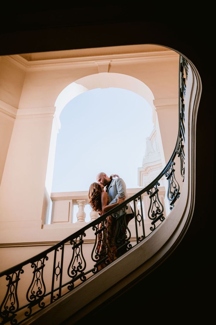 a bride and groom kissing on the stairs at their wedding reception in front of an arched doorway