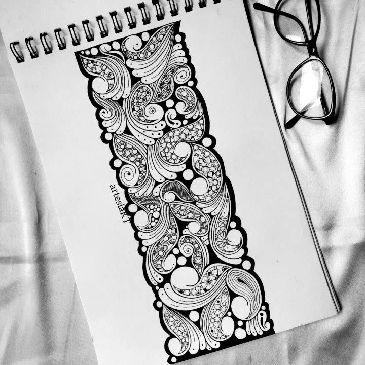 a spiral notebook with black and white doodles on it next to eyeglasses