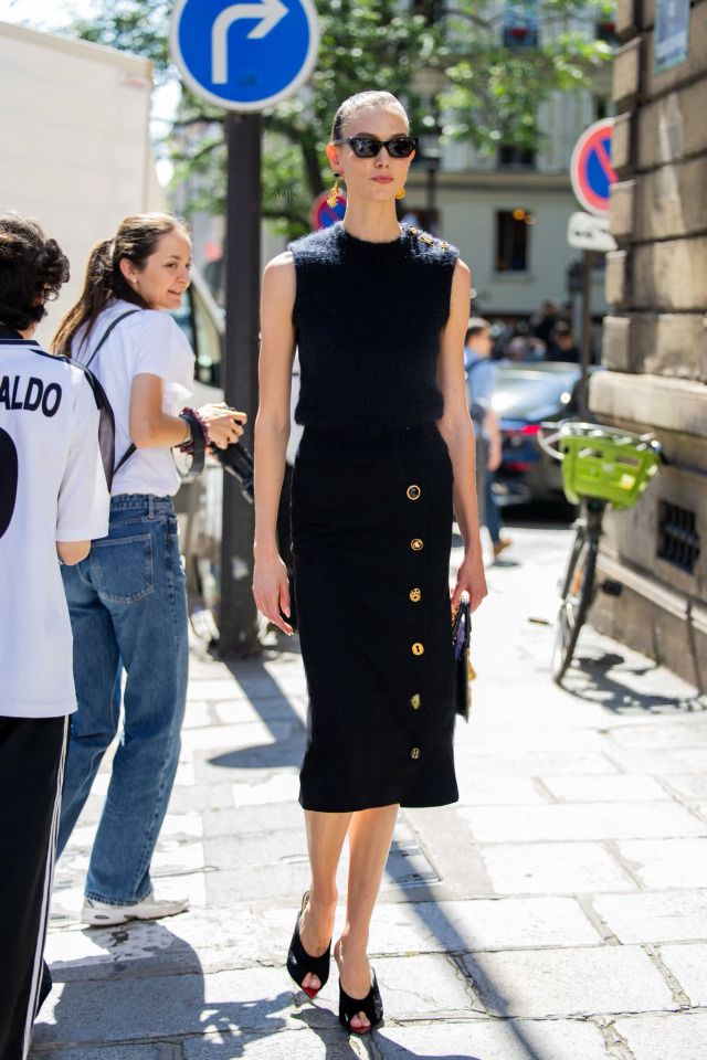 a woman is walking down the street wearing a black dress with buttons on her skirt