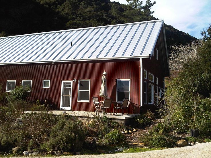 a red house with a metal roof and two chairs on the front porch next to it