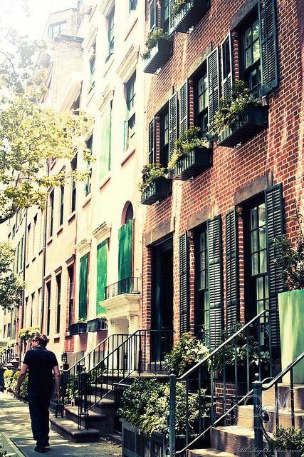 a man walking down the sidewalk in front of some tall buildings with green shutters