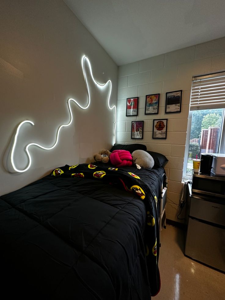 a room with a bed, desk and pictures on the wall above it is lit up by neon lights