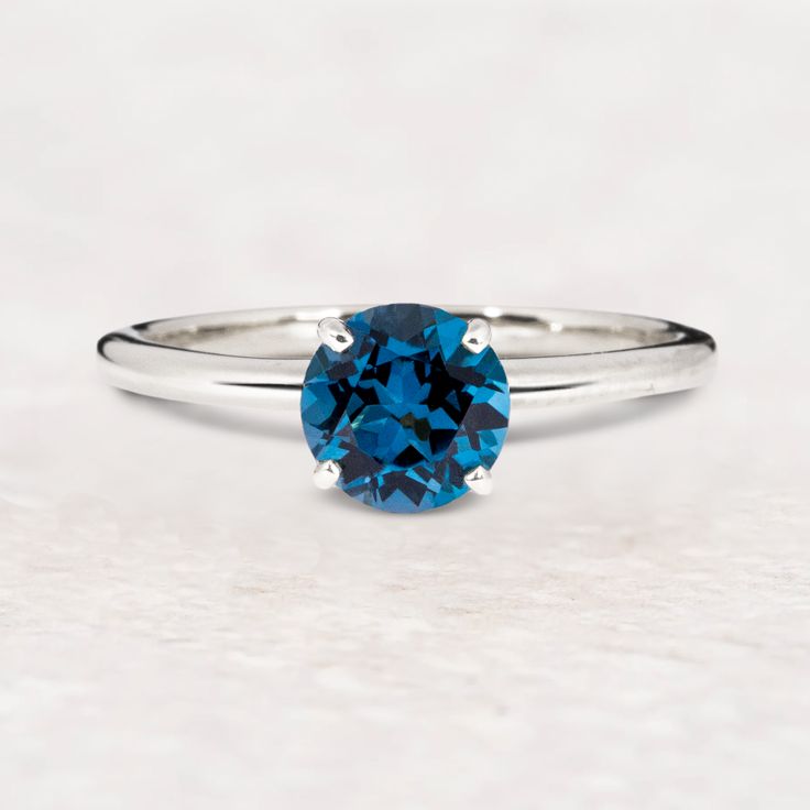 a blue diamond ring sitting on top of a white surface with the center stone in the middle