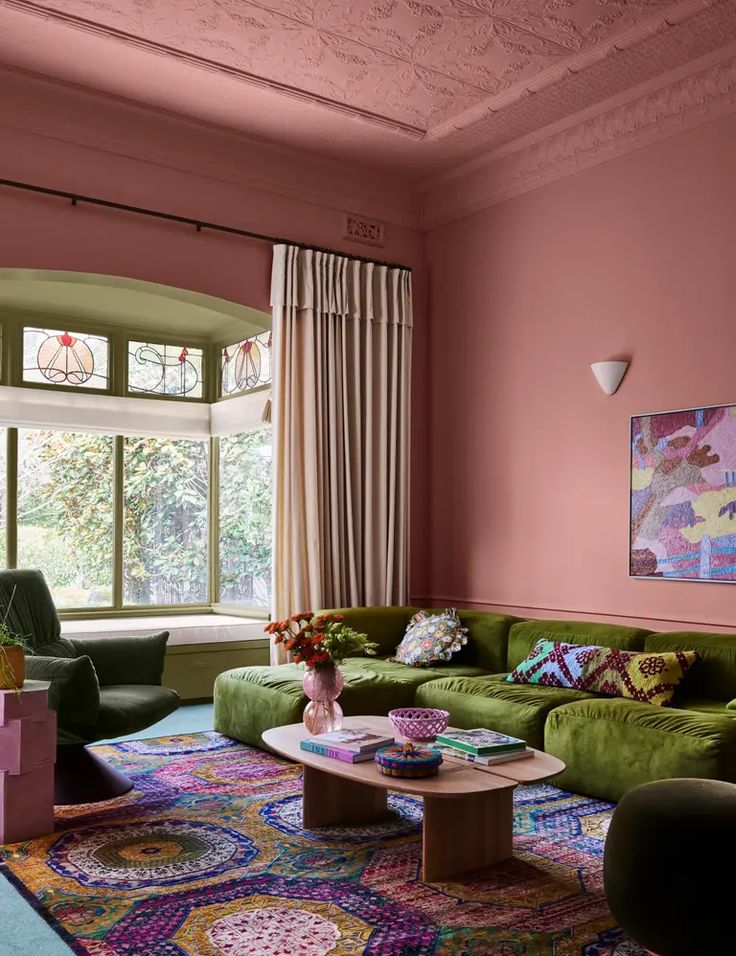 a living room with pink walls, green couches and colorful rug on the floor