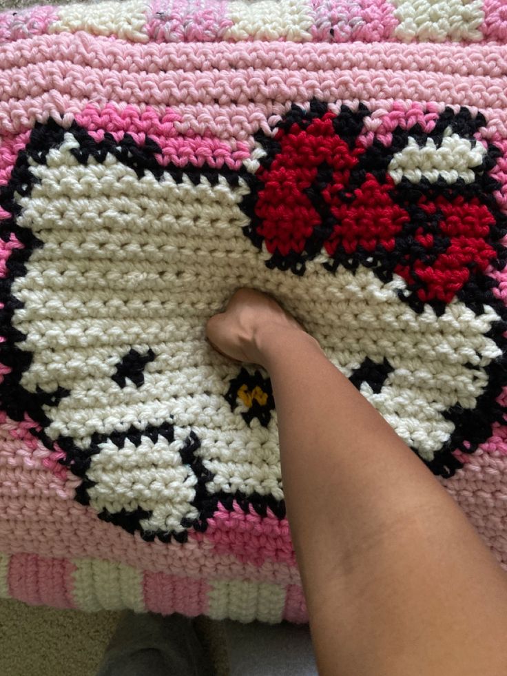 someone is crocheting a hello kitty blanket on the floor with their foot propped up