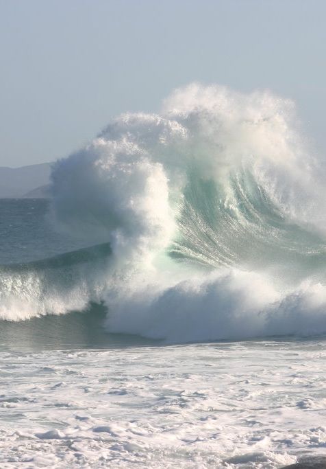 a large wave crashing into the ocean on a sunny day