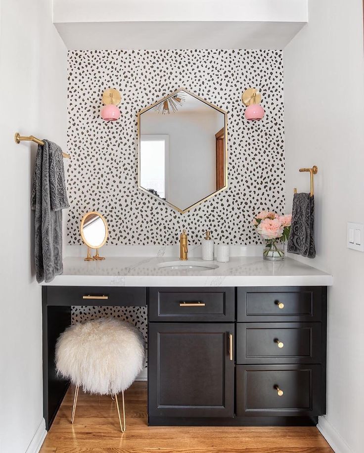 a white and black bathroom with gold accents on the mirror above the vanity, along with a stool in front of it