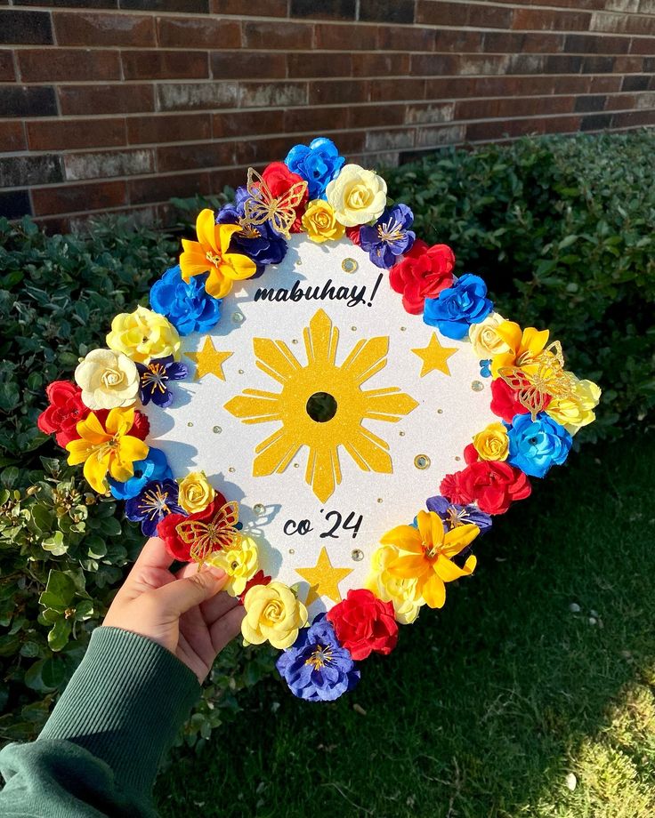 a hand holding up a graduation cap decorated with paper flowers and the words maatuhday written on it