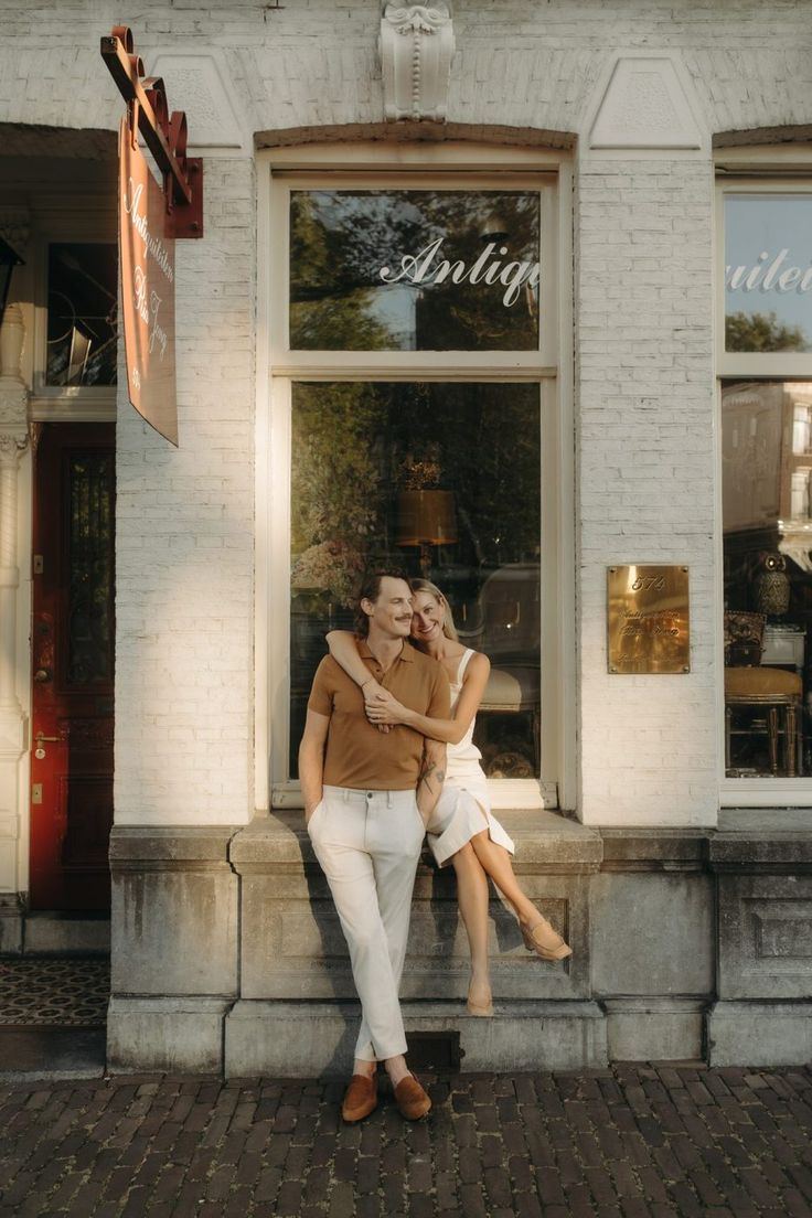 a man and woman sitting in front of a store with their arms around each other