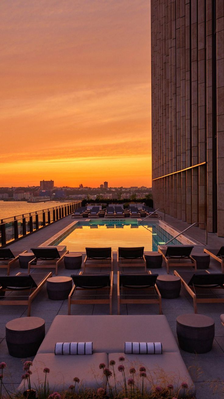 the sun is setting over an outdoor pool with lounge chairs and tables in front of it