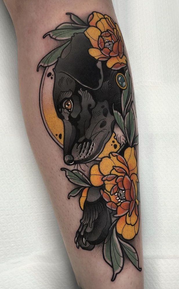 a woman's leg with flowers and a black dog on the bottom half of it