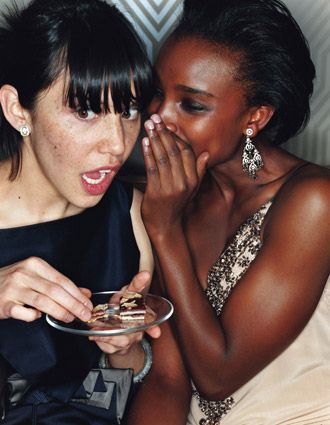 two women sitting next to each other and one holding a plate with food on it