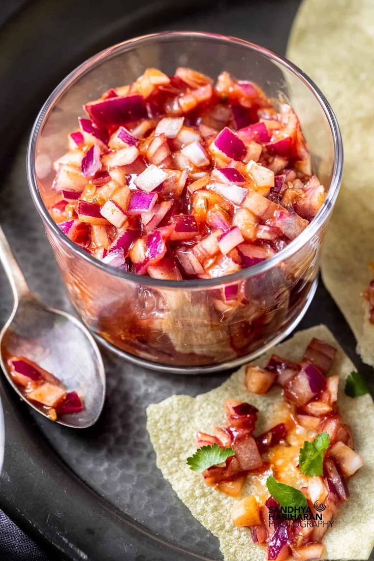 a glass bowl filled with salsa next to tortilla chips on a black plate