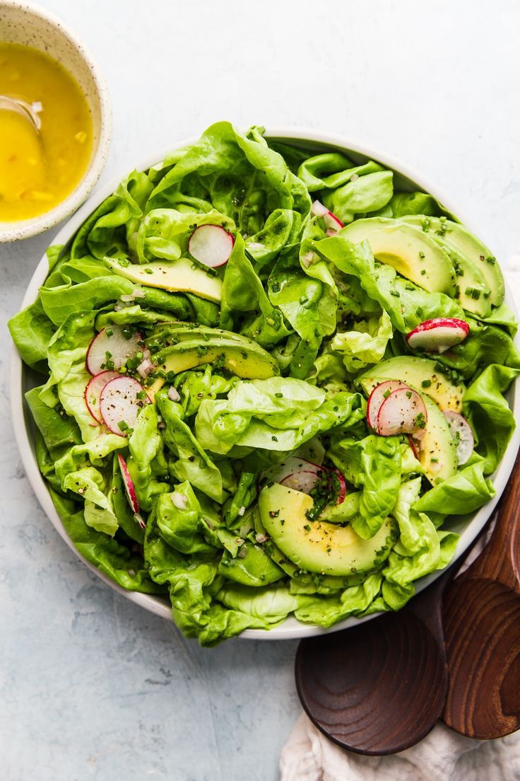 a bowl filled with lettuce and radishes next to a wooden spoon